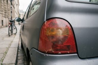 Feu arrière fissuré et jauni sur une petite voiture urbaine grise garée en ville